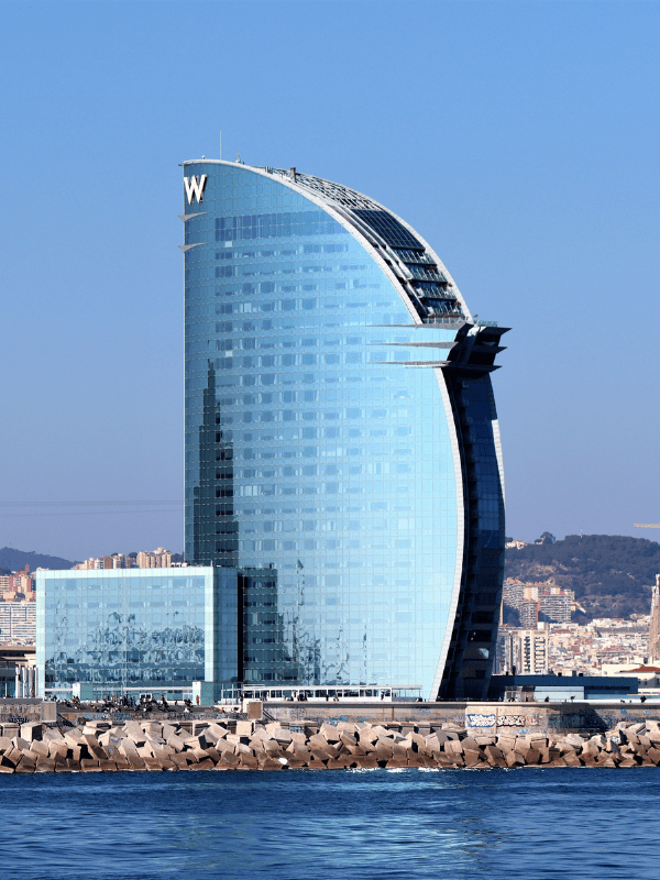 Vista del icónico Hotel W en el puerto de Barcelona, destacando un servicio de taxi disponible para traslados desde y hacia el puerto.